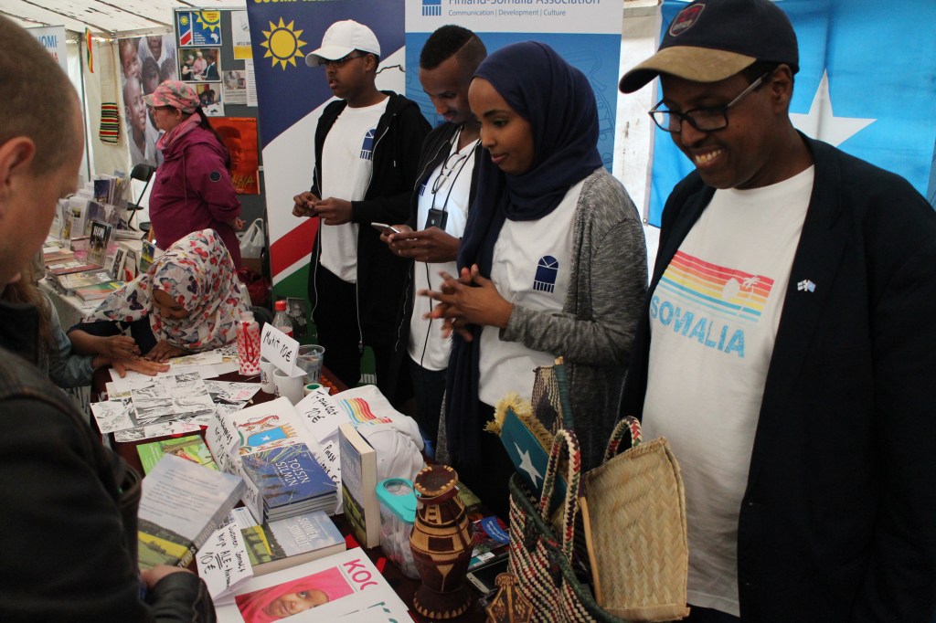 Kuvassa Seuran vapaaehtoiset esittelevät toimintaa Maailma kylässä- festivaalilla, esitteitä ja tuotteita pöydällä