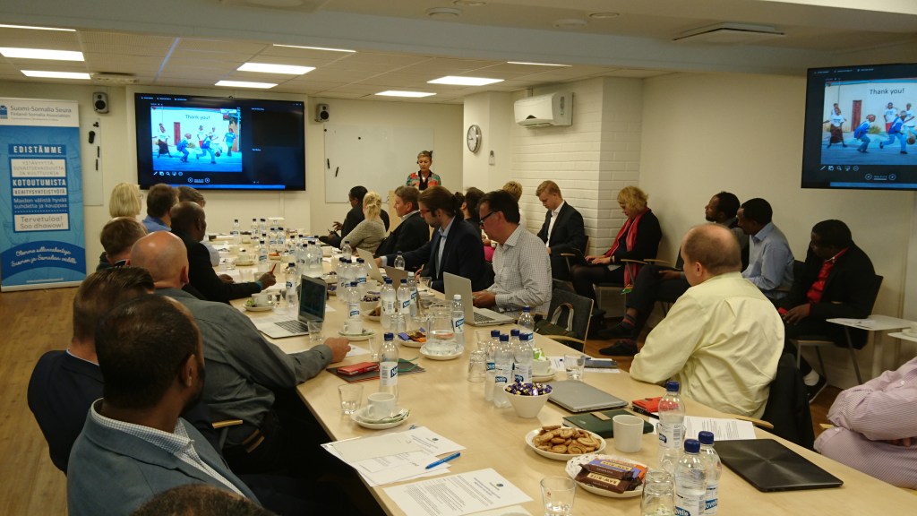 Kuva Finnish-Somali Business Council -kokouksesta, ihmiset istuvat pitkän pöydän ääressä ja katsovat diaesitystä