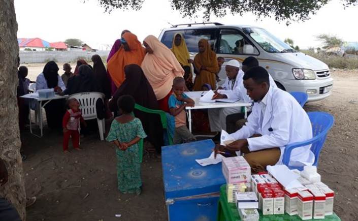Lääkärin vastaanotto, kuvassa naisia lapsineen sekä lääkäri ja sairaanhoitovälineitä