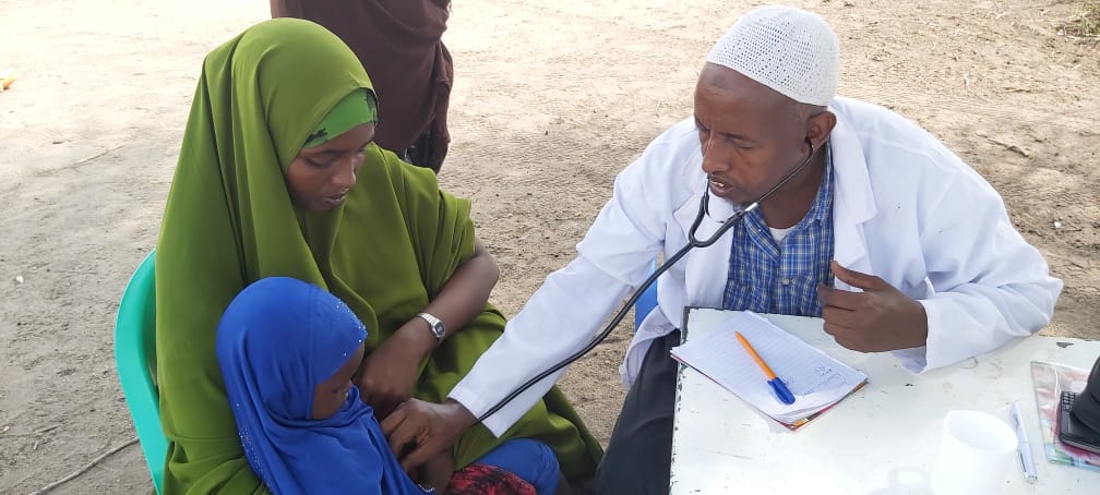 Mieslääkäri tutkii stetoskoopilla lapsipotilasta, joka istuu äidin sylissä.